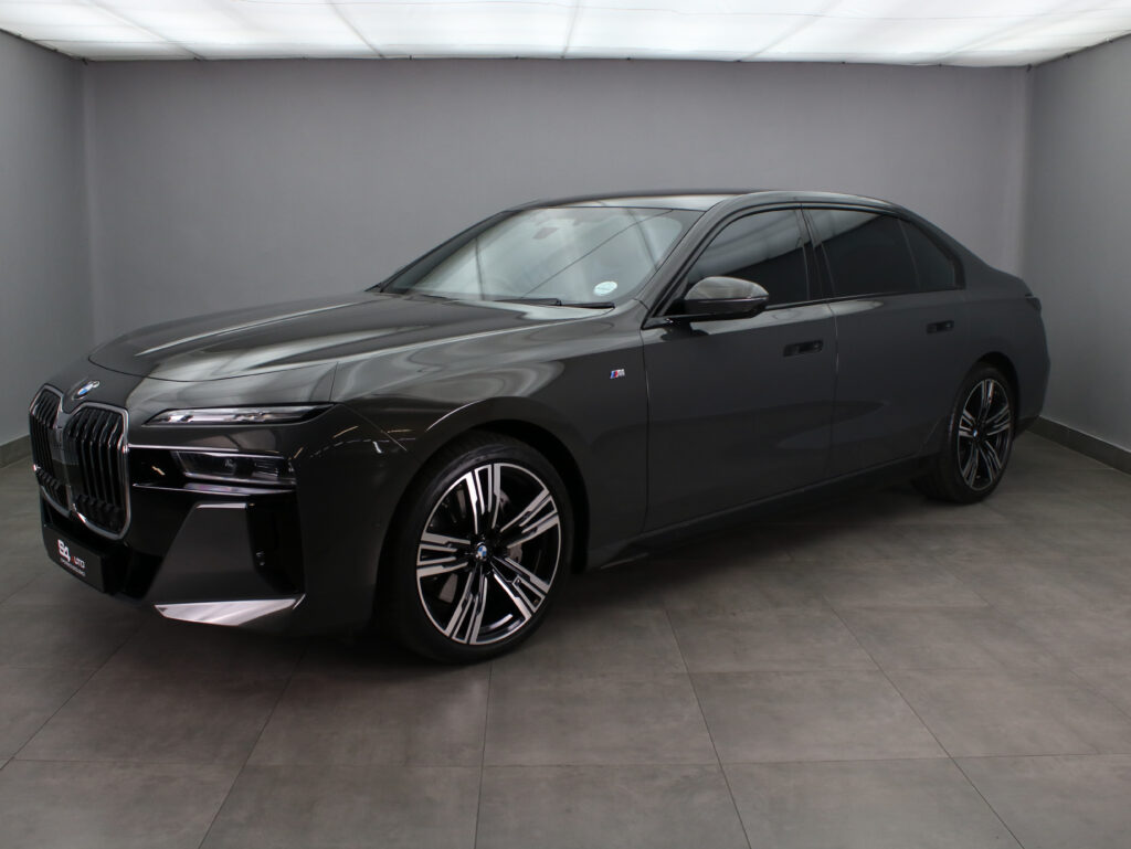 Three-quarter front view of a dark gray BMW sedan with large kidney grilles, in a showroom with gray walls and tiled floor