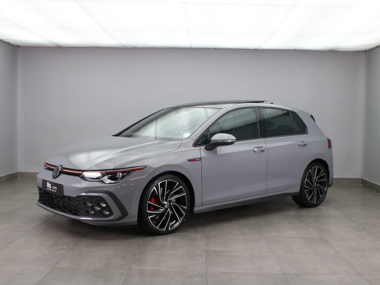 Gray Volkswagen Golf GTI hatchback in a studio setting, featuring red accent stripe, large alloy wheels, and red brake calipers.