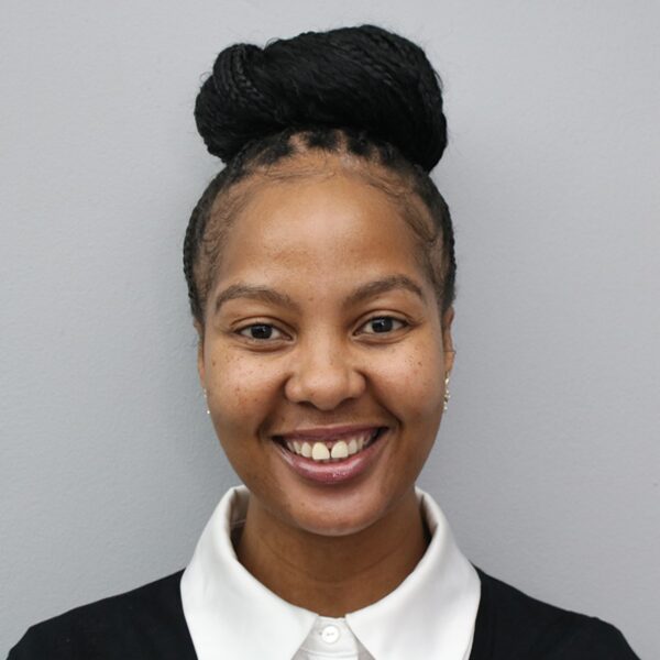 Smiling woman with a high braided bun, wearing a white collared shirt and black cardigan, against a gray background.