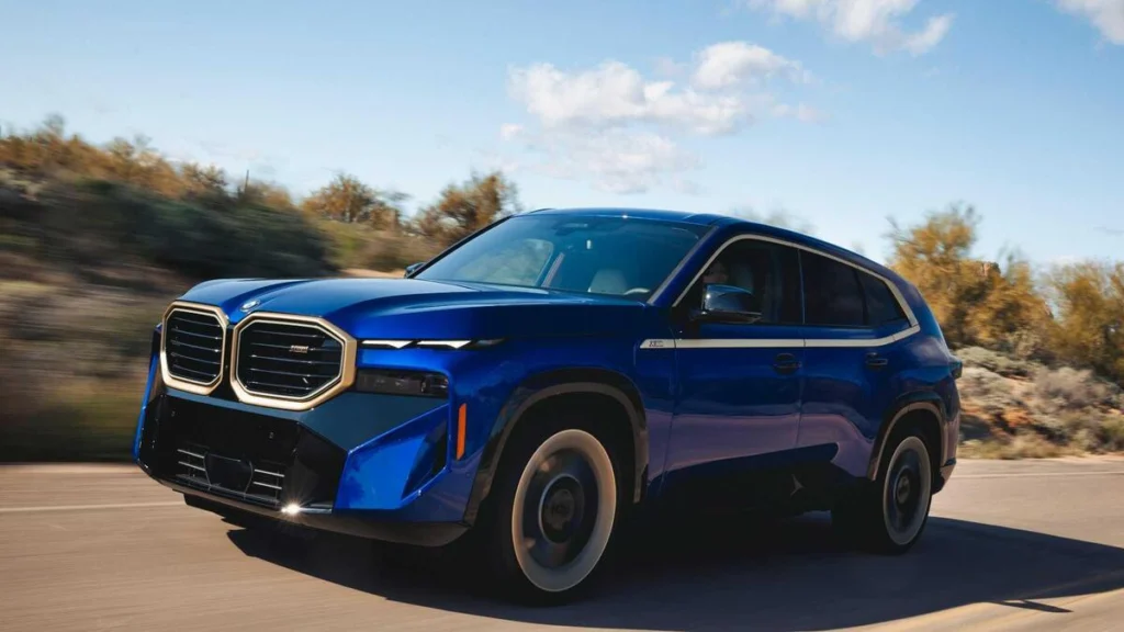 Blue SUV driving on a sunny road, front angled view showing bold grille and modern headlights