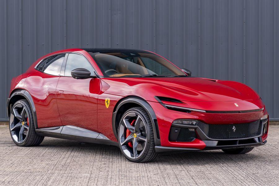 Red Ferrari sports car parked on a paved lot in front of a gray metal wall.